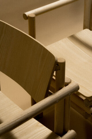 Nahaufnahme von hellen Holzstühlen mit schlichtem, minimalistischem Design, bei der die Armlehnen, Rückenlehnen und Sitzflächen überlappend angeordnet sind.