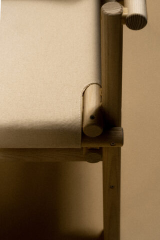 Nahaufnahme einer Struktur aus hellem Holz und Sperrholz mit abgerundeten Kanten, zylindrischer Stütze und einem glatten, minimalistischen Design vor einem beigen Hintergrund.