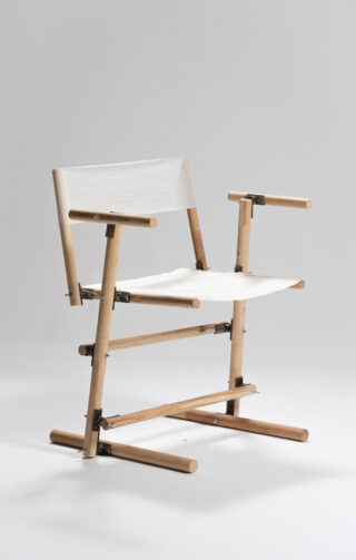 Ein minimalistischer Holzstuhl mit Sitzfläche und Rückenlehne aus weißem Stoff, sichtbaren Metallverbindungen und einem einfachen, eckigen Design vor einem schlichten hellen Hintergrund.