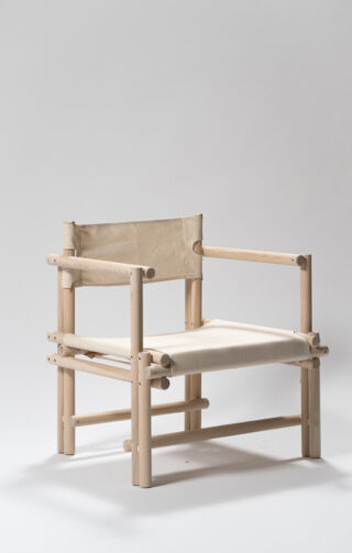 Ein minimalistischer Holzstuhl mit natürlichem Finish, Sitzfläche und Rückenlehne aus Segeltuch vor einem schlichten hellen Hintergrund.