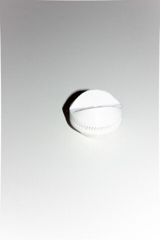 Ein rundes, weißes Objekt, das einer Tablette oder einem Puck ähnelt, mit einer Ritzlinie und einem dezent gekerbten Rand liegt auf einer schlichten weißen Oberfläche.