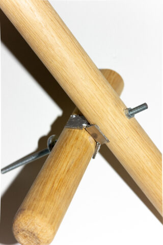 Drei Holzdübel kreuzen sich und sind durch Metallklammern, Bolzen und Flügelmuttern vor einem schlichten weißen Hintergrund verbunden.