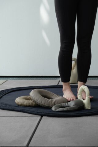 Person steht barfuß auf einer dunklen Matte neben mehreren weich gepolsterten Gymnastikringen, nur ihre Beine sind sichtbar.