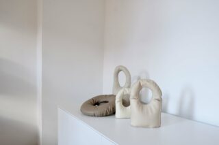 Drei beige- und hellbraune Skulpturenobjekte mit kreisförmigen Ausschnitten werden auf einem weißen Schrank vor einer schlichten weißen Wand ausgestellt.