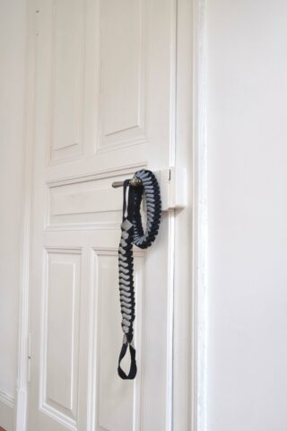 Ein geflochtenes schwarz-graues Seil mit einem Griff ist über den Metallgriff einer geschlossenen weißen Holztür geschlungen.