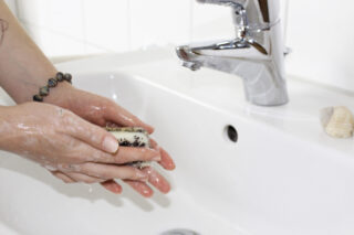 Person wäscht ihre Hände in einem Waschbecken mit einen Seifenstück.