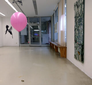 Innenraum, rechts hängt eine Skulptur aus Spiegelscherben an der Wand, im Vordergrund schwebt ein rosafarbener Luftballon.