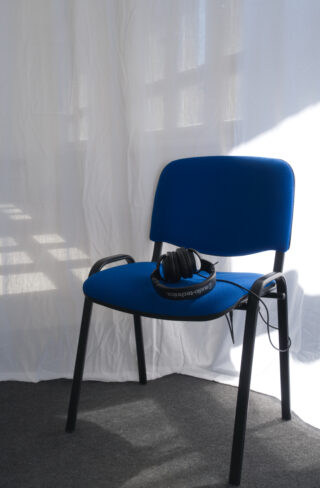 Ein Paar Audio-Technica-Kopfhörer liegt auf einem blauen Stuhl mit schwarzen Beinen, der auf einem dunklen Teppich vor einem weißen Vorhang steht.