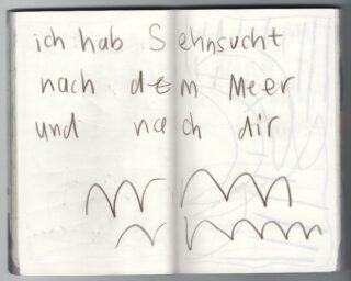 Auf einer handgeschriebenen deutschen Notiz steht: „Ich habe Sehnsucht nach dem Meer und nach dir“, wobei unter dem Text Wellenlinien gezeichnet sind, die an Wellen erinnern.