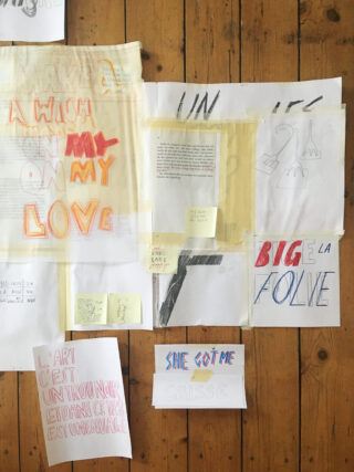 Eine Sammlung handgezeichneter Textkunstwerke, Skizzen und Notizen ist auf einen Holzboden geklebt und enthält Sätze auf Englisch und Französisch in verschiedenfarbigen Markern und Bleistiften.