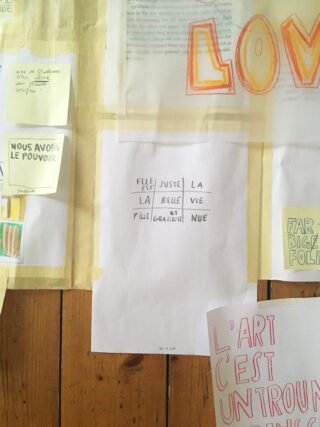 Eine Wand mit verschiedenen handgeschriebenen und gedruckten Papieren auf Französisch, darunter Notizen, Zeichnungen und Sätze, die auf einen cremefarbenen Hintergrund geklebt sind.