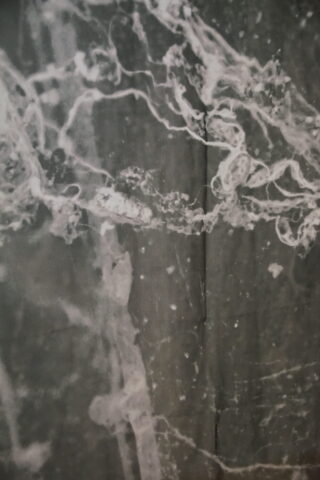 Nahaufnahme einer grauen Oberfläche mit weißen, unregelmäßigen, aderartigen Linien und Mustern, die an Marmor- oder Mineralstrukturen erinnern.