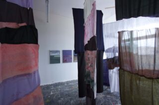 Ein Raum mit bemalten Stoffpaneelen, die von der Decke hängen, und zwei Landschaftsgemälden an der weißen Wand im Hintergrund.