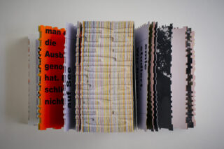 Eine Draufsicht auf ein offenes Buch mit gezackten, unregelmäßig geschnittenen Seiten in verschiedenen Farben und gedrucktem Text, vertikal angeordnet vor einem weißen Hintergrund.