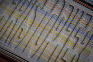 Eine Nahaufnahme gestapelter Papierblätter mit bunten, gewellten Linien und kräftigen geprägten Formen, die auf der Oberfläche eine erhabene Textur erzeugen.