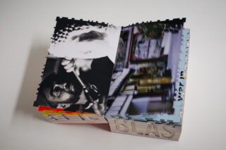 Ein offenes Kunstbuch mit gezackten Seitenrändern, das ein Schwarzweißfoto eines Geigers und ein verschwommenes, buntes Bild eines Raumes zeigt.