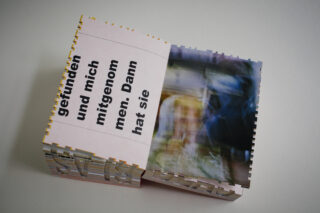 Ein aufgeschlagenes Buch mit einem unscharfen Foto auf der rechten Seite und deutschem Text auf der linken Seite, platziert auf einer hellen Unterlage.