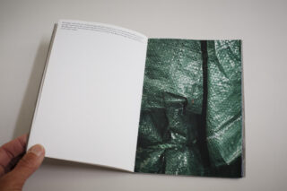 Ein offenes Buch mit einer weitgehend leeren linken Seite mit Text oben und einer rechten Seite mit einer Nahaufnahme eines grünen gewebten Kunststoffmaterials.