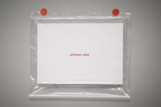 Eine weiße Karte mit dem deutschen Text „schützen, alles“ ist in einer durchsichtigen Plastikhülle eingeschlossen und mit zwei roten Magneten an einer grauen Wand befestigt.
