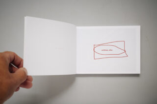 Eine Hand hält ein minimalistisches Buch aufgeschlagen; auf der rechten Seite ist eine rote abstrakte Form mit dem deutschen Text „schütten, alles“ zu sehen, die linke Seite ist fast leer.