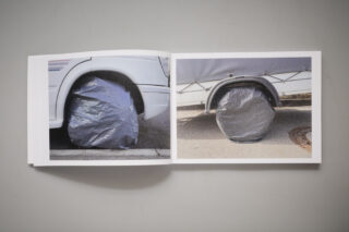 In einem aufgeschlagenen Buch sind zwei Fotos von Fahrzeugrädern mit grauen Schutzhüllen zu sehen. Das linke Foto zeigt ein Autorad, das rechte ein Anhängerrad.