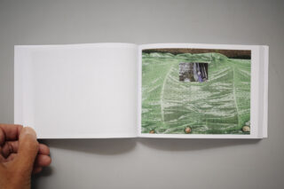 Ein offenes Buch zeigt ein Foto eines grünen, perforierten Stoffes mit einem kleinen rechteckigen Fenster und Objekten entlang der Unterkante.