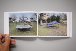 Ein offenes Buch zeigt zwei Fotos von Trampolinen in Rasenflächen, die jeweils mit Planen abgedeckt sind; im Hintergrund sind Bäume und Außenanlagen zu sehen.