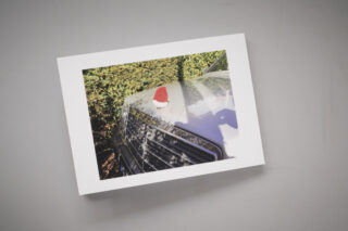 Ein Foto einer Motorhaube eines Autos mit einer kleinen rot-weißen Weihnachtsmannmütze darauf, präsentiert auf einer weißen Fläche.