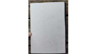 Der Finger einer Person hält ein leeres weißes Blatt Papier aufrecht gegen eine Holzoberfläche.