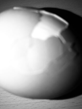 Eine Nahaufnahme eines aufgeschlagenen Eis in Schwarzweiß, das auf einer Holzoberfläche liegt, wobei die starke Beleuchtung Reflexionen und Schatten erzeugt.