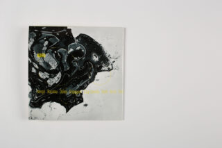 Auf einer schlichten weißen Oberfläche befindet sich ein quadratisches Heft mit abstrakten, marmorartigen schwarz-weißen Kunstwerken und gelbem Text.