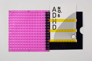 Eine Zeitschrift mit der Aufschrift „ADHD Nr. 5“ gleitet teilweise aus einer schwarz-weißen Hülle, neben einem durchscheinend rosafarbenen, strukturierten Kunststoffeinband mit Metallverschlüssen.