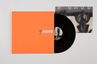 Eine schwarze Vinyl-Schallplatte, teilweise aus einer orangefarbenen Hülle mit der Aufschrift „ADHD“ herausgelöst, mit einem Einleger darüber, der ein abstraktes Kunstwerk zeigt.