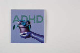 Eine Hand hält eine Topfpflanze mit Sonnenbrille vor einem violetten Hintergrund, auf dem in großen grünen Buchstaben das Wort „ADHS“ steht.