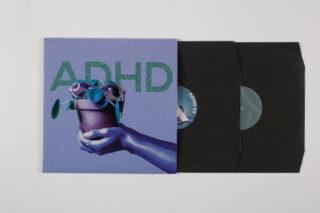 Eine Vinyl-Schallplatte, die teilweise aus einer schwarzen Hülle herausragt, neben einem Albumcover mit der Aufschrift „ADHS“ und dem Bild einer Hand, die eine Topfpflanze hält und eine Sonnenbrille trägt.