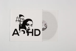 Eine teilweise aus einer weißen Hülle gezogene Vinyl-Schallplatte mit schwarzen abstrakten Gesichtern und dem aufgedruckten Text „ADHS“ auf dem Cover.