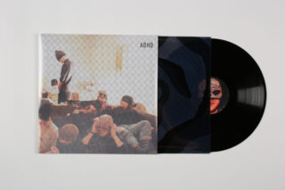Eine teilweise aus ihrer Hülle gezogene Vinyl-Schallplatte, auf der eine Gruppe maskierter Menschen zu sehen ist. Auf dem Cover ist der Text „ADHS“ zu sehen.