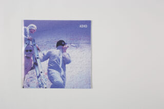 Auf einer weißen Fläche befindet sich ein quadratisches Objekt mit dem Bild von zwei Personen in Winterkleidung, die Skier halten, und dem Text „ADHS“ in der oberen rechten Ecke.