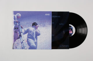 Eine teilweise aus ihrer Hülle gerissene Vinyl-Schallplatte, auf der vor einem verschneiten Hintergrund zwei Personen in Winterkleidung mit Skiern in der Hand zu sehen sind.