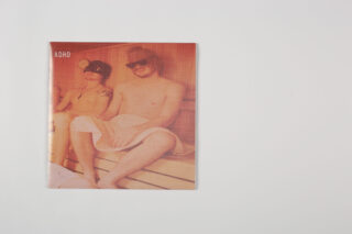 Ein Foto von zwei Personen, die in einer Sauna sitzen, beide tragen Handtücher und Sonnenbrillen, mit einem orangefarbenen Farbton über dem Bild und dem Wort „ADHS“ in der oberen linken Ecke.