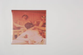 Ein Foto, das drei zusammensitzende Personen zeigt, die teilweise verdeckt sind und durch eine transparente, gemusterte Abdeckung vor einem schlichten weißen Hintergrund betrachtet werden können.