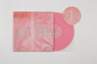 Auf weißem Untergrund sind eine rosafarbene Vinyl-Schallplatte, ein passendes Albumcover mit dem Schriftzug „ADHD“ aus Strasssteinen und ein runder Papiereinleger angeordnet.
