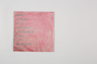 Ein rosafarbenes quadratisches Tuch mit einer Liste von Wörtern, die mit grauem Faden aufgestickt sind, darunter „MAMORI“, „BACALAU“, „BOLO“, „GRIPAOU“, „OLAY CAMILA“, „STULI“, „FIFI PI“, „TIBERINOUR“ und „TULLI“.