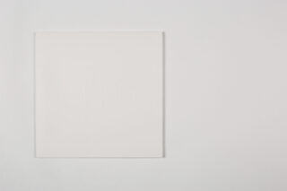 Ein weißes quadratisches Objekt mit schwach geprägten Linien und Formen befindet sich auf einem schlichten weißen Hintergrund, etwas links von der Mitte positioniert.