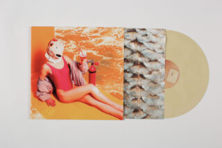 Eine beige Vinyl-Schallplatte, teilweise in einer Hülle, mit dem Coverbild einer Person in einem roten Badeanzug und einer Gasmaske, die mit einem Feuerlöscher vor einem orangefarbenen, abstrakten Hintergrund sitzt.