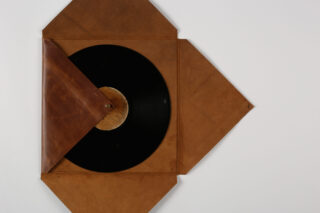 Eine schwarze Vinyl-Schallplatte war teilweise aus einer braunen Lederhülle gerutscht und auf einem schlichten weißen Hintergrund zu sehen.