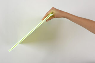 Eine Hand hält ein dünnes, leuchtendes, neongrünes rechteckiges Objekt schräg vor einem schlichten weißen Hintergrund.