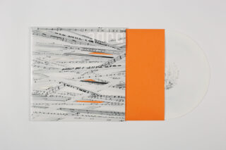 Eine durchsichtige Vinyl-Schallplatte, teilweise mit einer orangefarbenen Papierhülle und einer bedruckten Außenhülle mit schwarzen Musiknoten auf weißem Hintergrund bedeckt.
