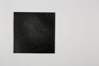 Auf der linken Seite eines schlichten hellgrauen Hintergrunds befindet sich ein schwarzes Quadrat mit weißen Sprenkeln, die Sternen ähneln.