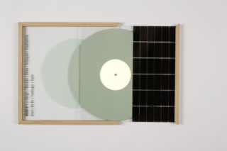 Eine durchscheinende Vinyl-Schallplatte ist teilweise aus einem Holzrahmen gerutscht, mit schwarzen Gitterkacheln auf der rechten Seite und vertikal gedrucktem Text entlang der linken Kante.